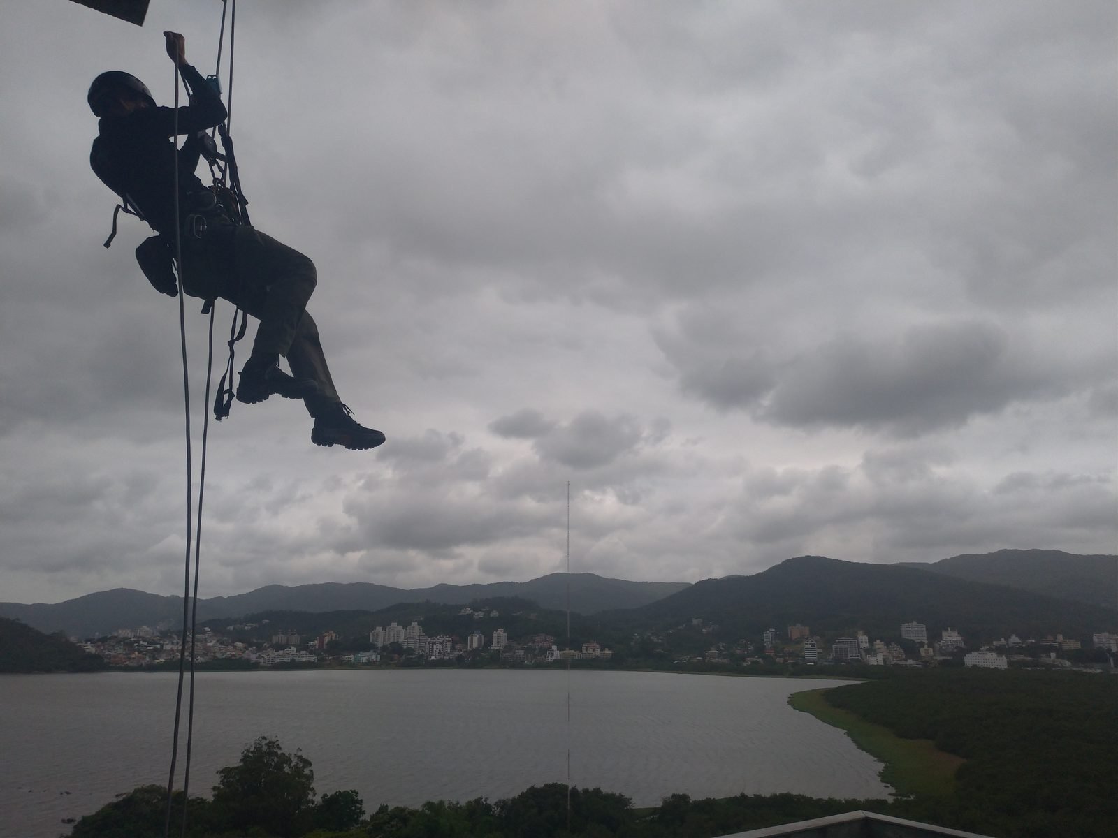 Profissional em descida por corda em edifício, com a Lagoa da Conceição ao fundo